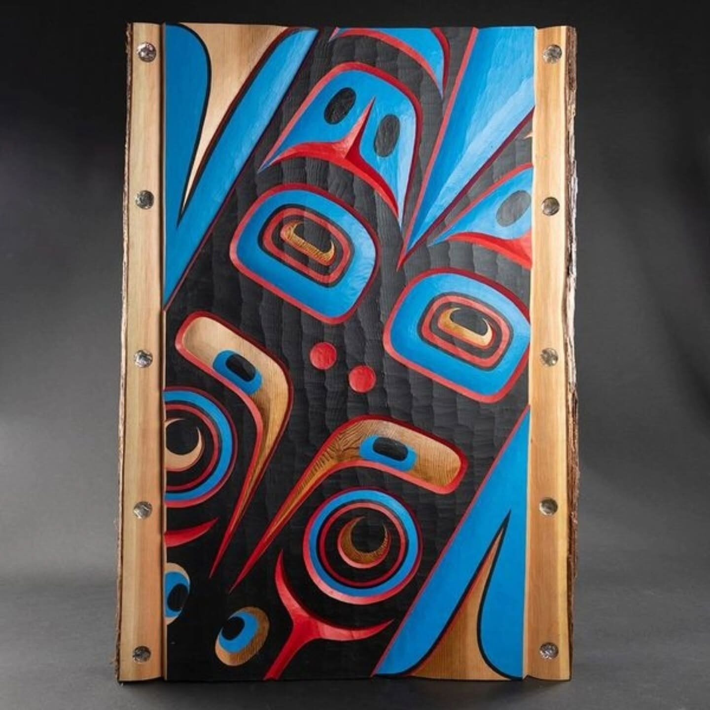 Live-edge cedar panel with an eagle carved in blue, red and black formline on a carved black field