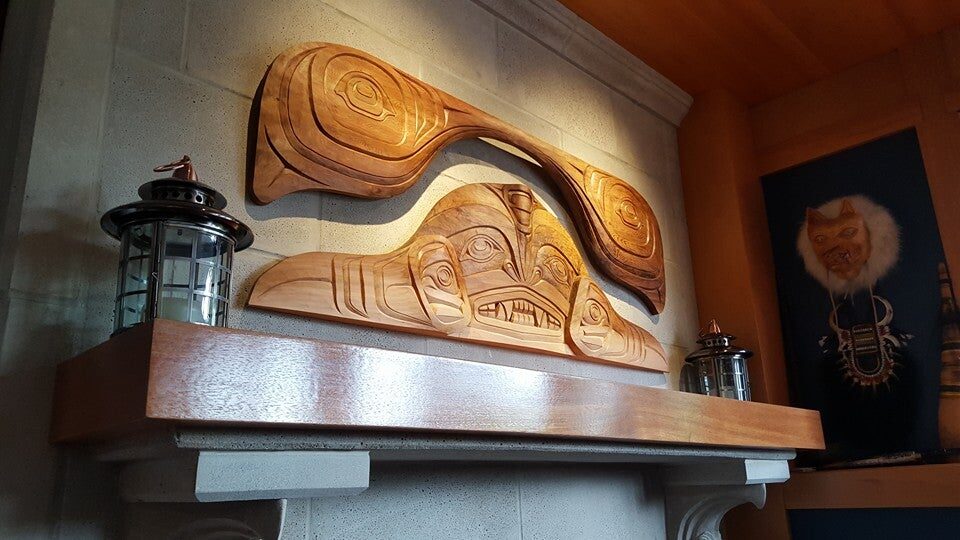 Carved cedar orca panel and carved beam mounted above a stone fireplace