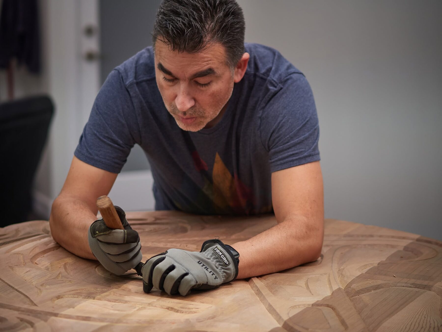 Jason Henry Hunt chiselling a large round cedar panel, wearing work gloves