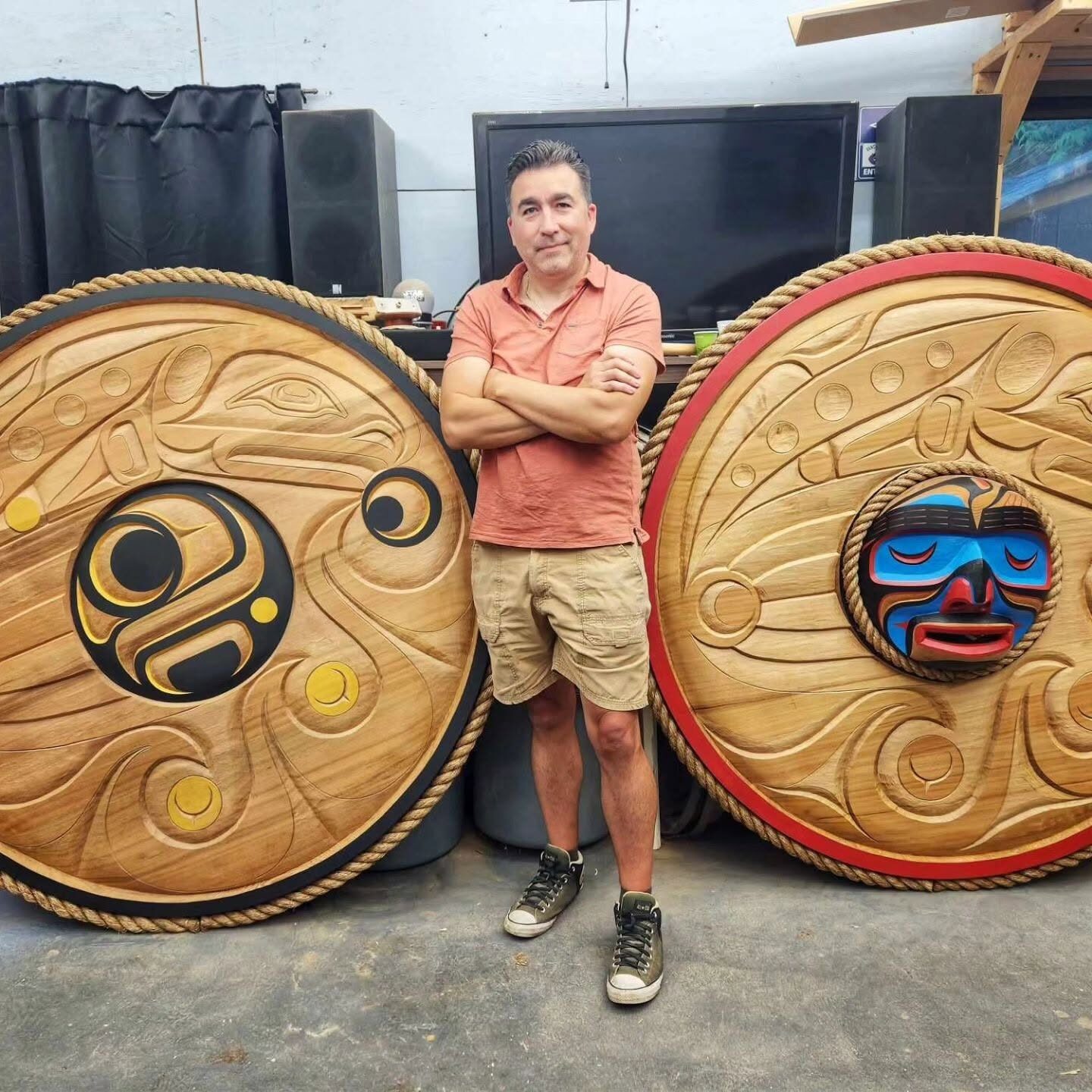 Jason Henry Hunt standing with arms crossed between two large rope-rimmed round panels in his workshop