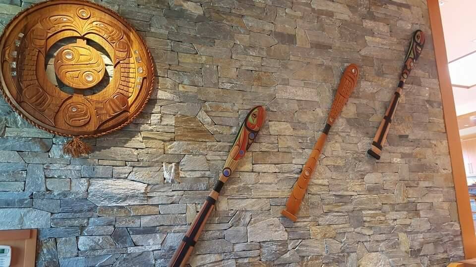 Three carved paddles and a round panel displayed on a stone wall