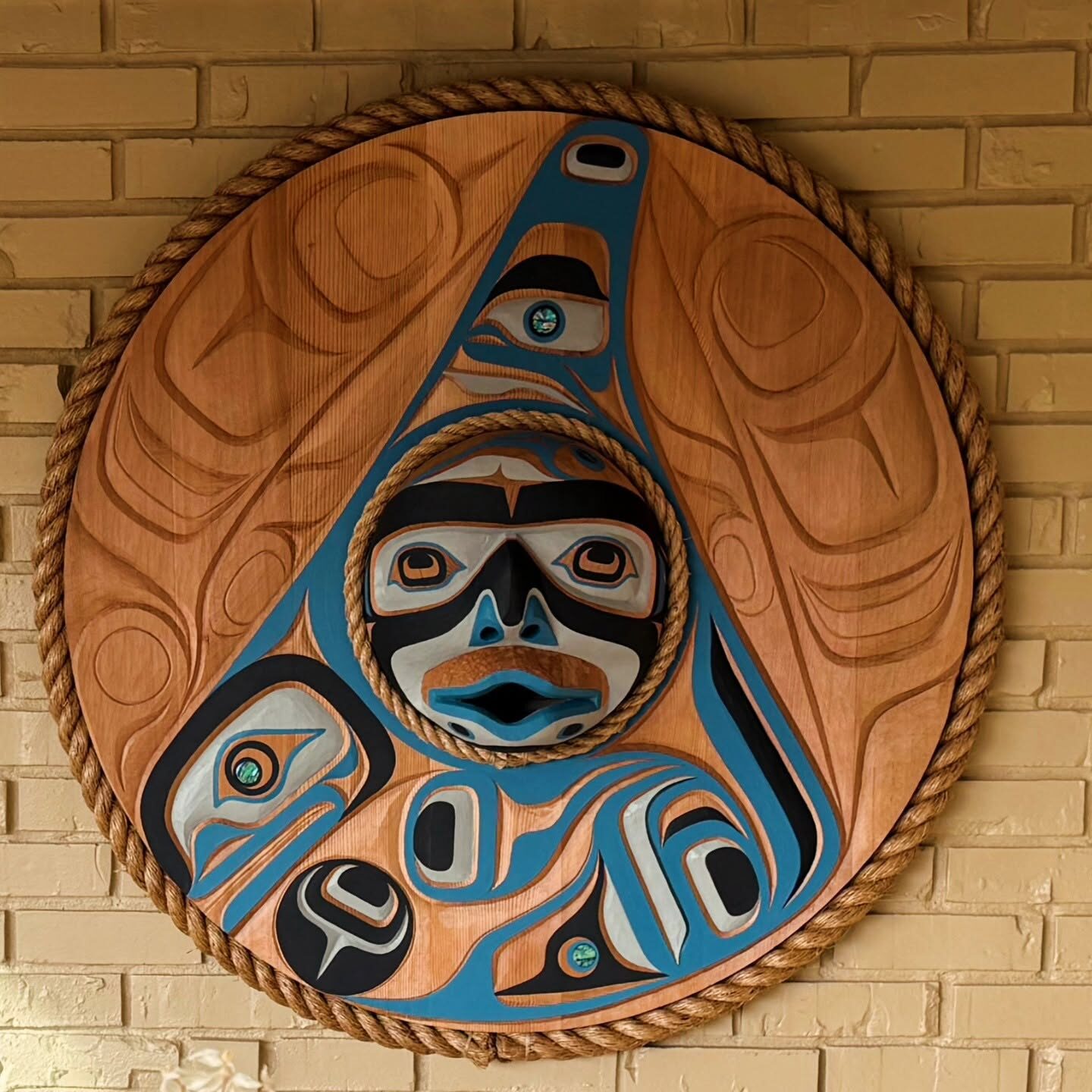 Teal and black moon mask round panel on a brick wall